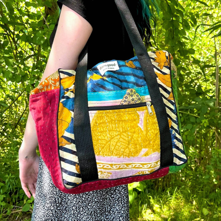 Colorful patchwork tote bag with black straps. Blue, yellow, and red patterns.