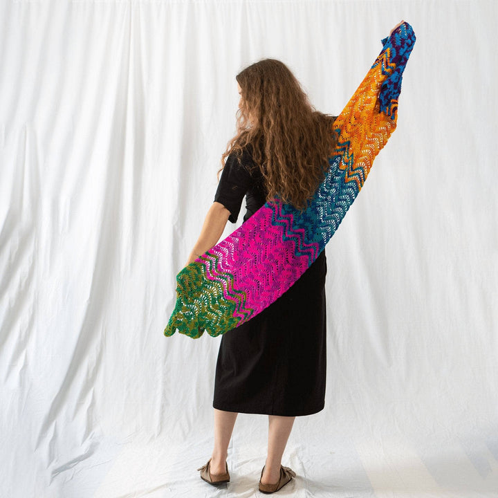 Founder Nicole holding wonderful waves crochet shawl outstretched behind her in front of a white background.