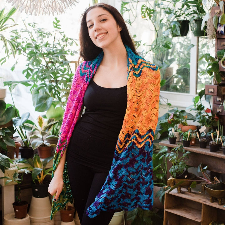 Model wearing wonderful waves wrap in rainbow with potted greenery in the background.