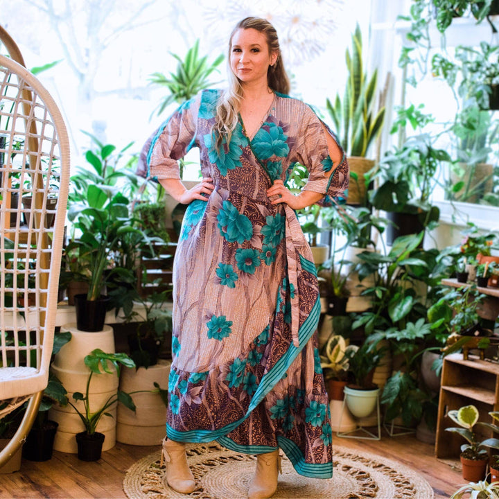 Woman in a floral dress stands in a room with potted plants on shelves and floor, on a round rug.