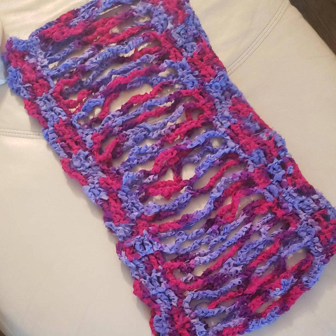 pink and purple crocheted cardigan top laying flat on a white chair