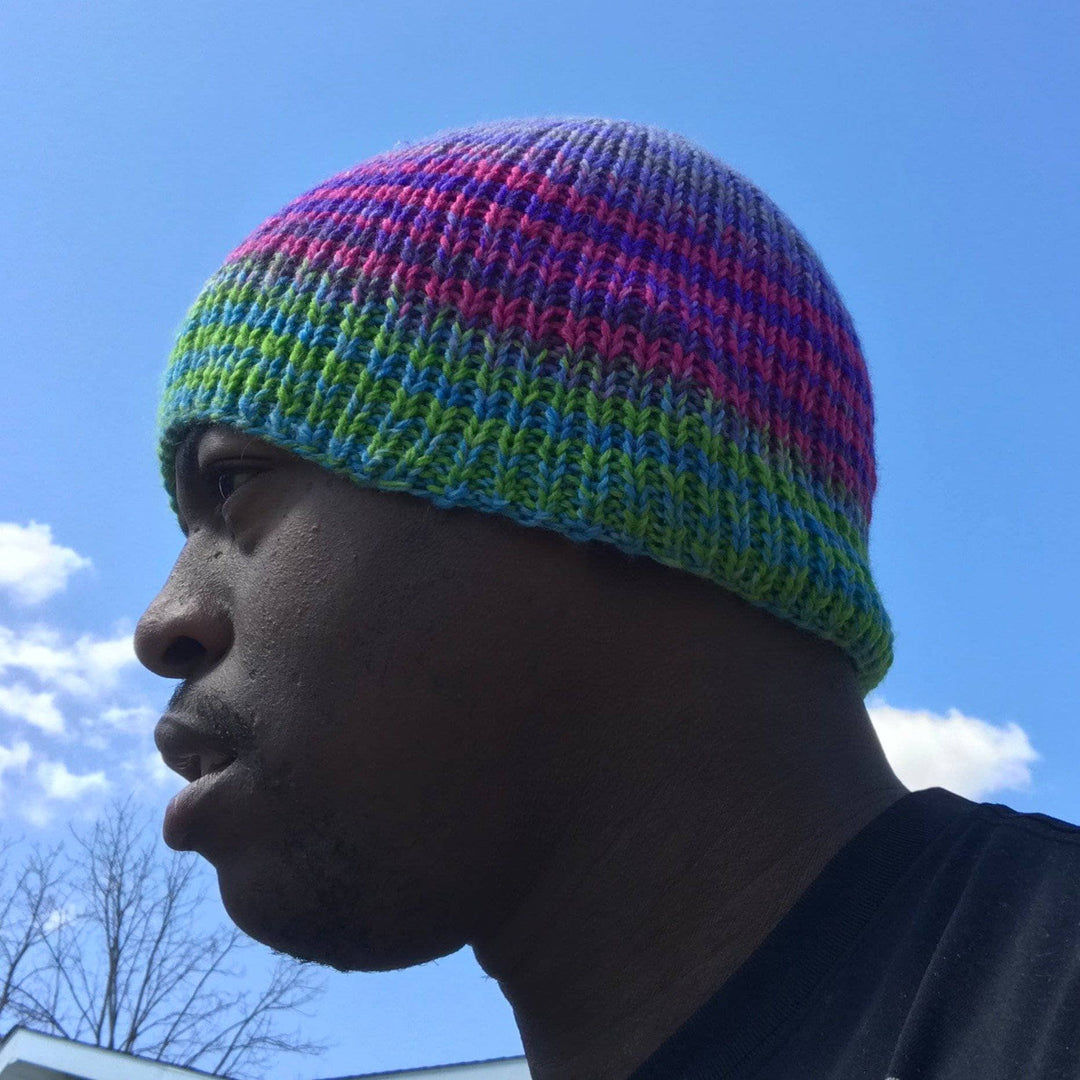 Pattern designer wearing a blue, green, pink and purple beanie outside