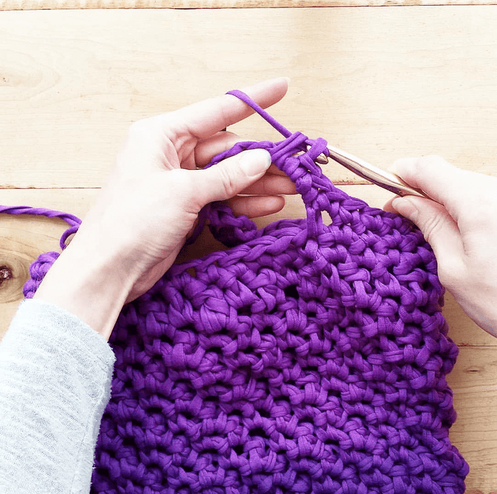 Woman's hands making the Violet Summer Tote Crochet Kit on a wooden background