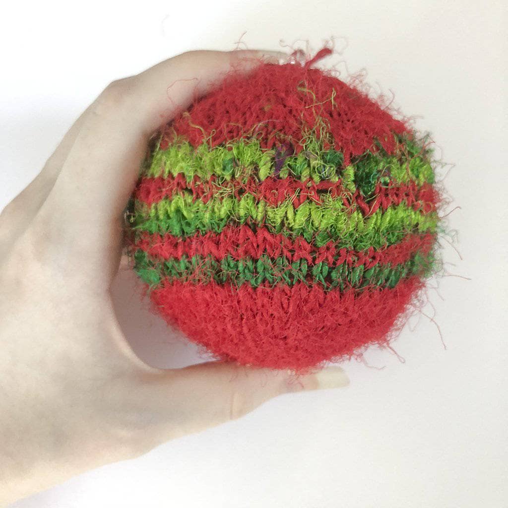 A person holding a red and green striped Christmas ornament on a white background