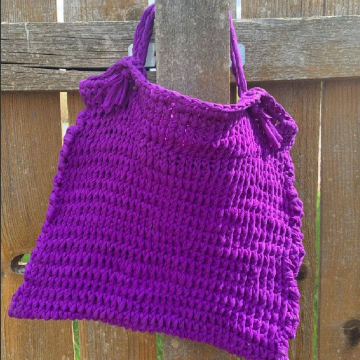 Knitted T-Shirt Bag in Pantone Ultra Violet hanging from a wooden fence