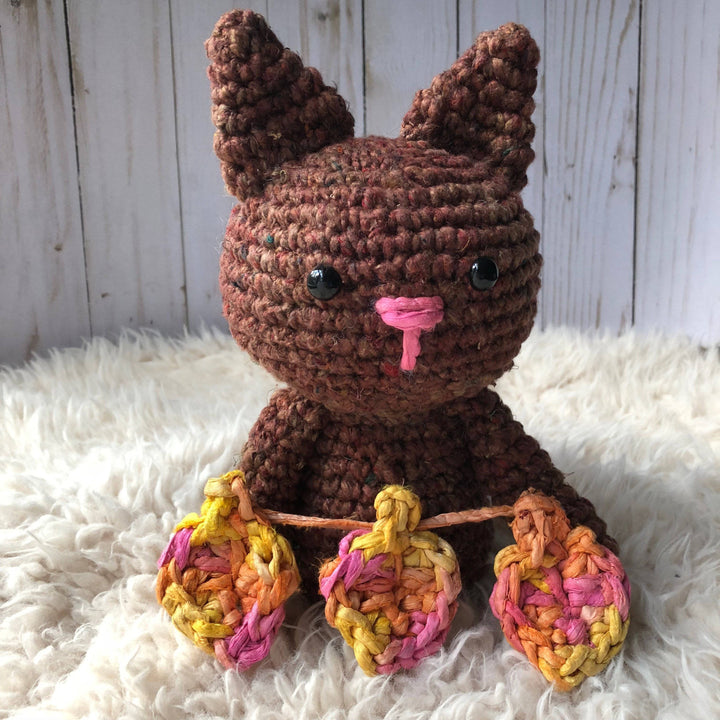 Amigurumi Crochet Cat in brown holding 3 crochet leaves sitting on a white furry surface