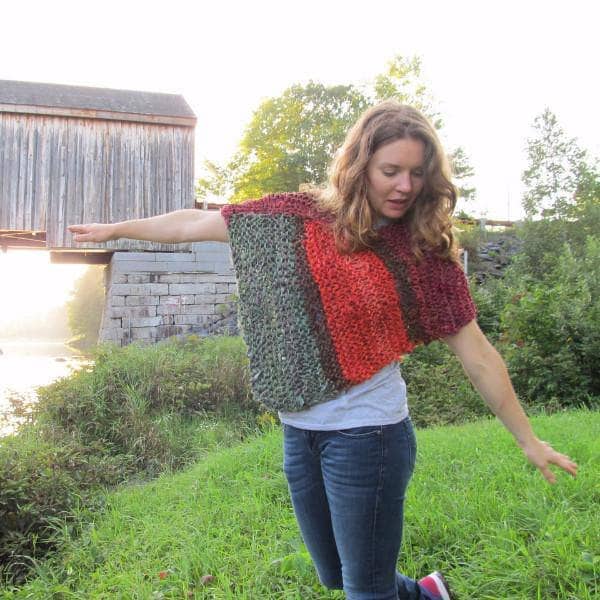 Woman wearing a red, orange, and green poncho and standing in front of a body of water