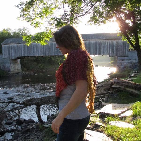 Woman wearing a red, orange, and green poncho and standing in front of a body of water