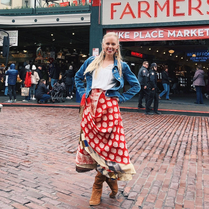 A woman in a red wrap skirt and denim jacket at a farmer's market.