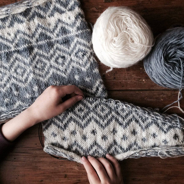 The Bjerge Pillow kit next to two yarn balls on a wooden background with woman's hands