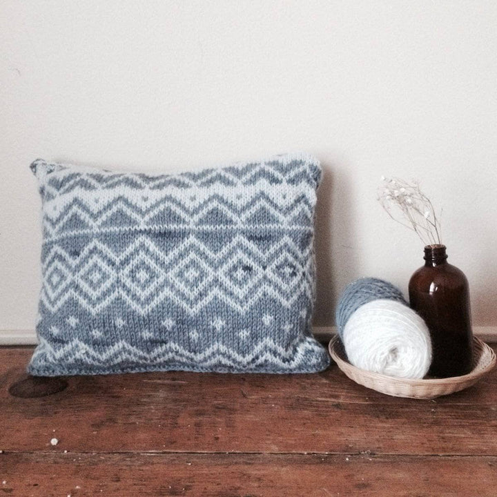 The Bjerge Pillow next to two yarn balls on a wooden background