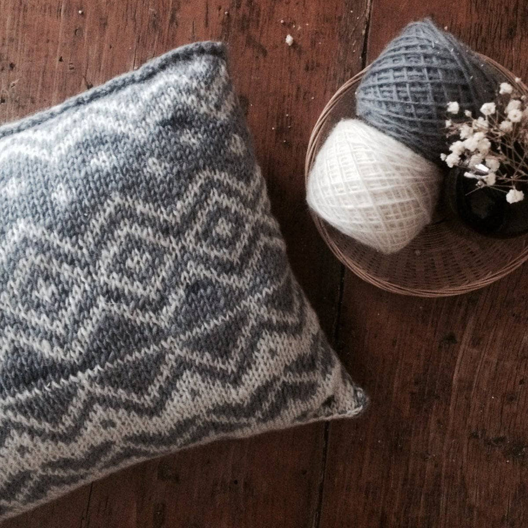 The Bjerge Pillow next to two yarn balls on a wooden background