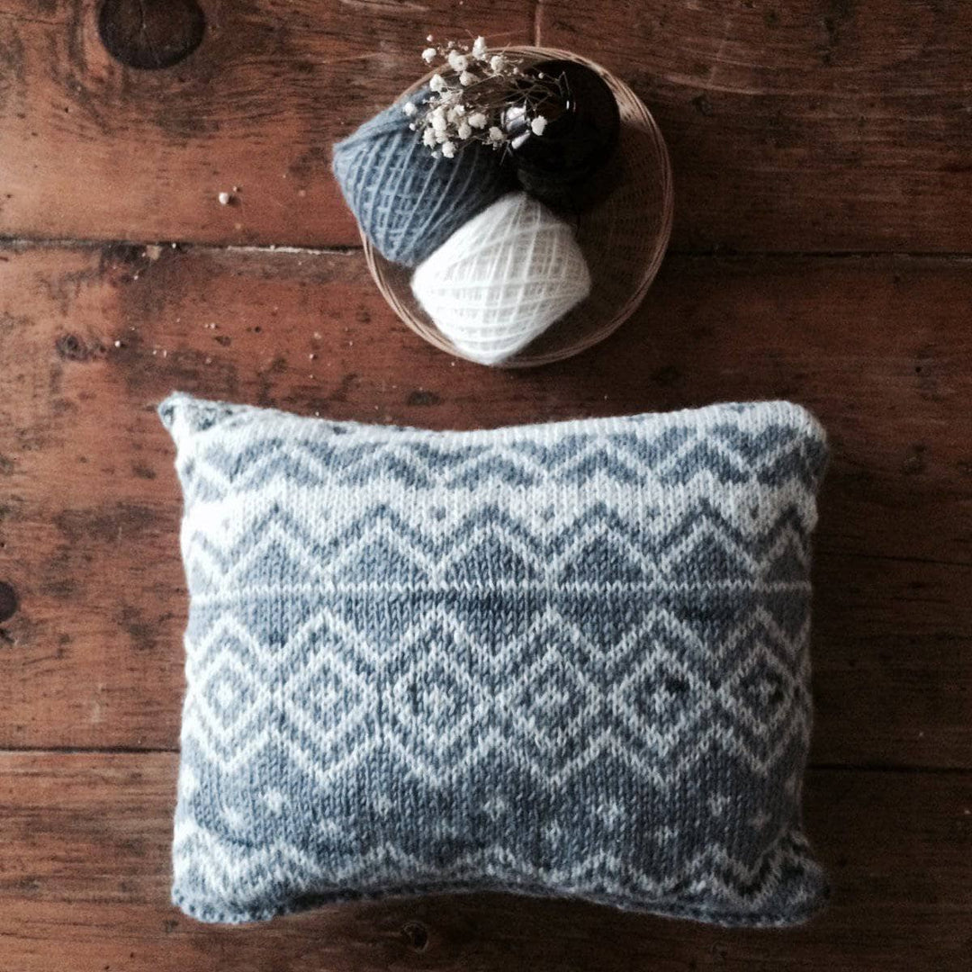 The Bjerge Pillow next to two yarn balls on a wooden background